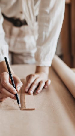 Lady in white outfit drawing clothing samples. Woman in beige blouse and pants creates garments patterns on paper sheet